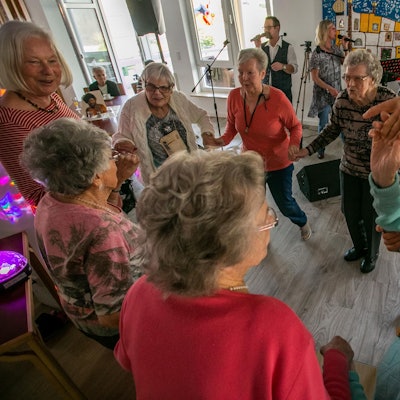 Senioren und Seniorinnen tanzen zu Schlagermusik in einem Partyraum.