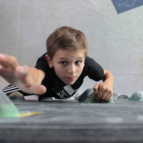 Ein Junge klettert an einer Boulderwand nach oben auf die Kamera zu.
