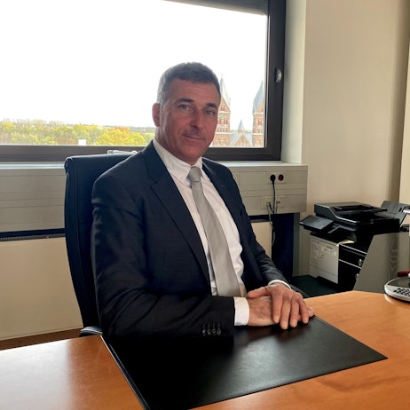 Ralph Manzke an seinem ersten Arbeitstag als Bürgermeister der Stadt Wesseling. Er sitzt mit übereinander gelegten Händen an seinem Schreibtisch und blickt in die Kamera.