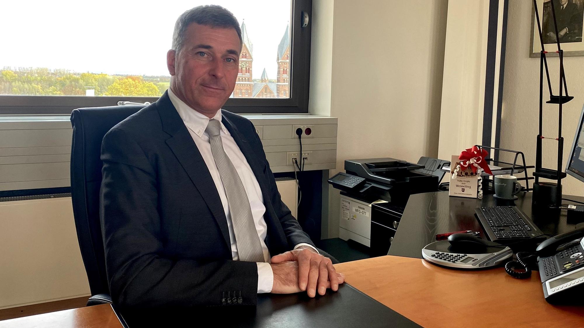 Ralph Manzke an seinem ersten Arbeitstag als Bürgermeister der Stadt Wesseling. Er sitzt mit übereinander gelegten Händen an seinem Schreibtisch und blickt in die Kamera.