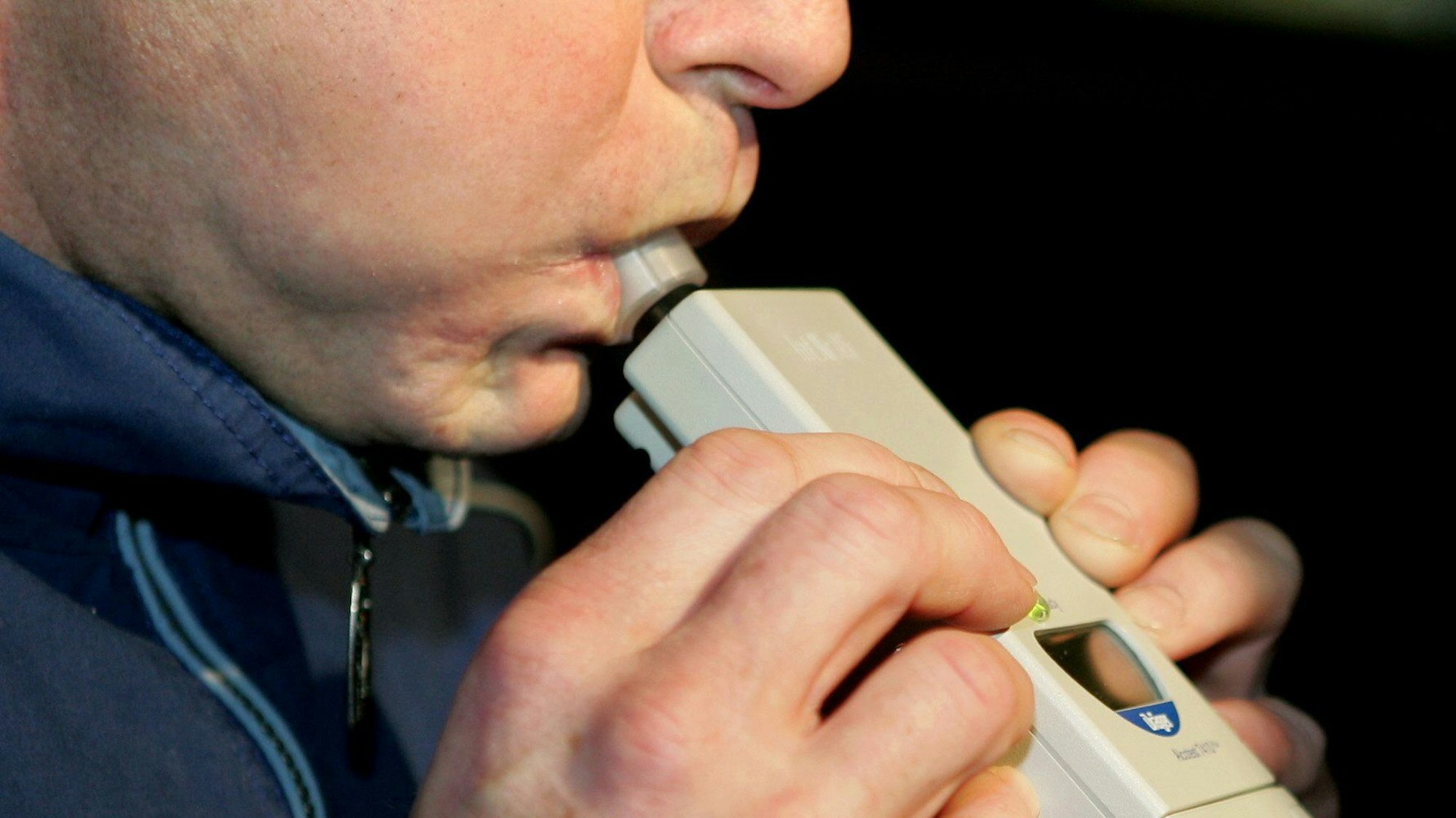 Das Bild zeigt eine Person, die in ein Alkoholtest-Gerät pustet.