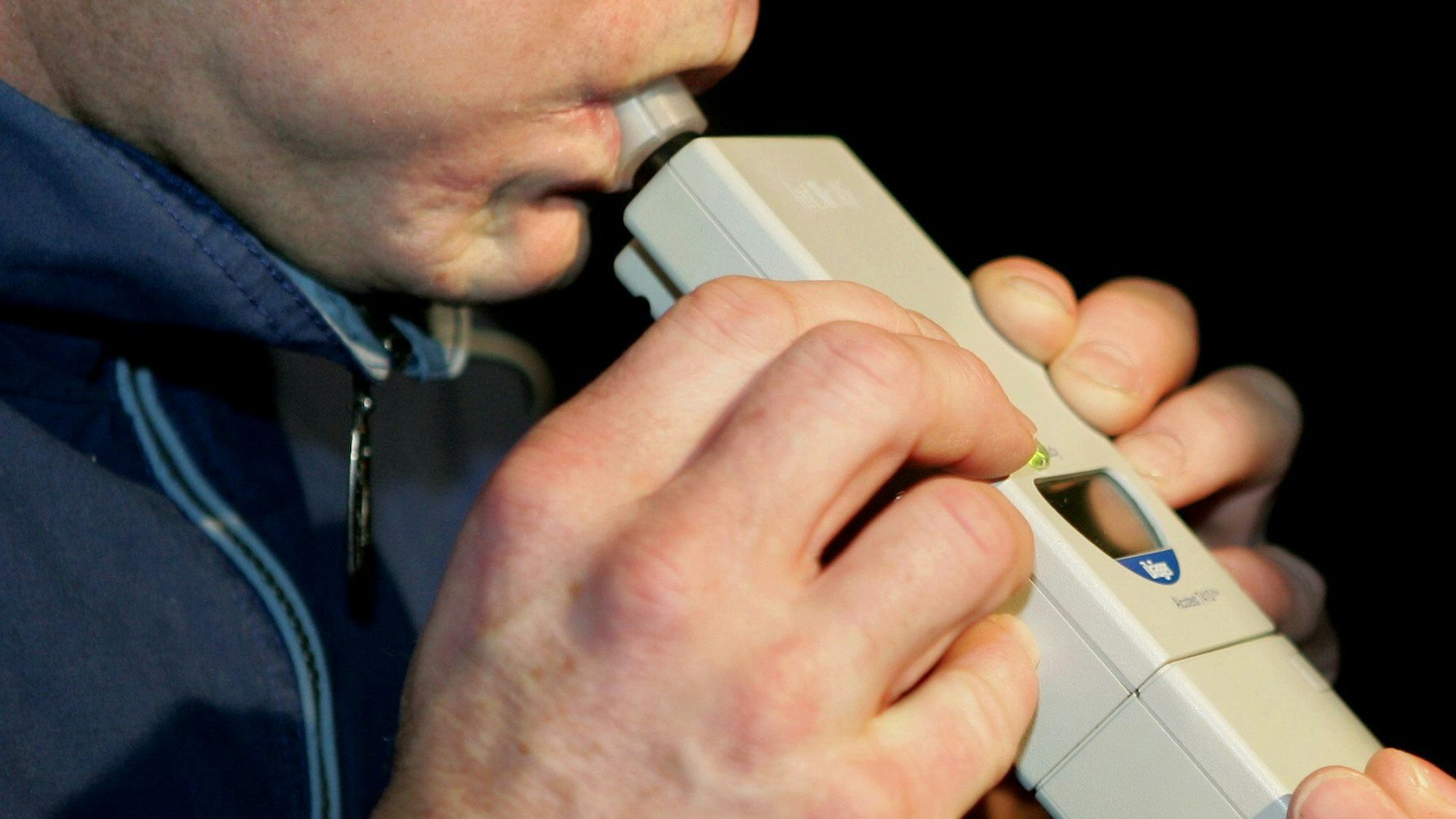 Das Bild zeigt einen Mann, der in ein Alkoholtestgerät pustet.