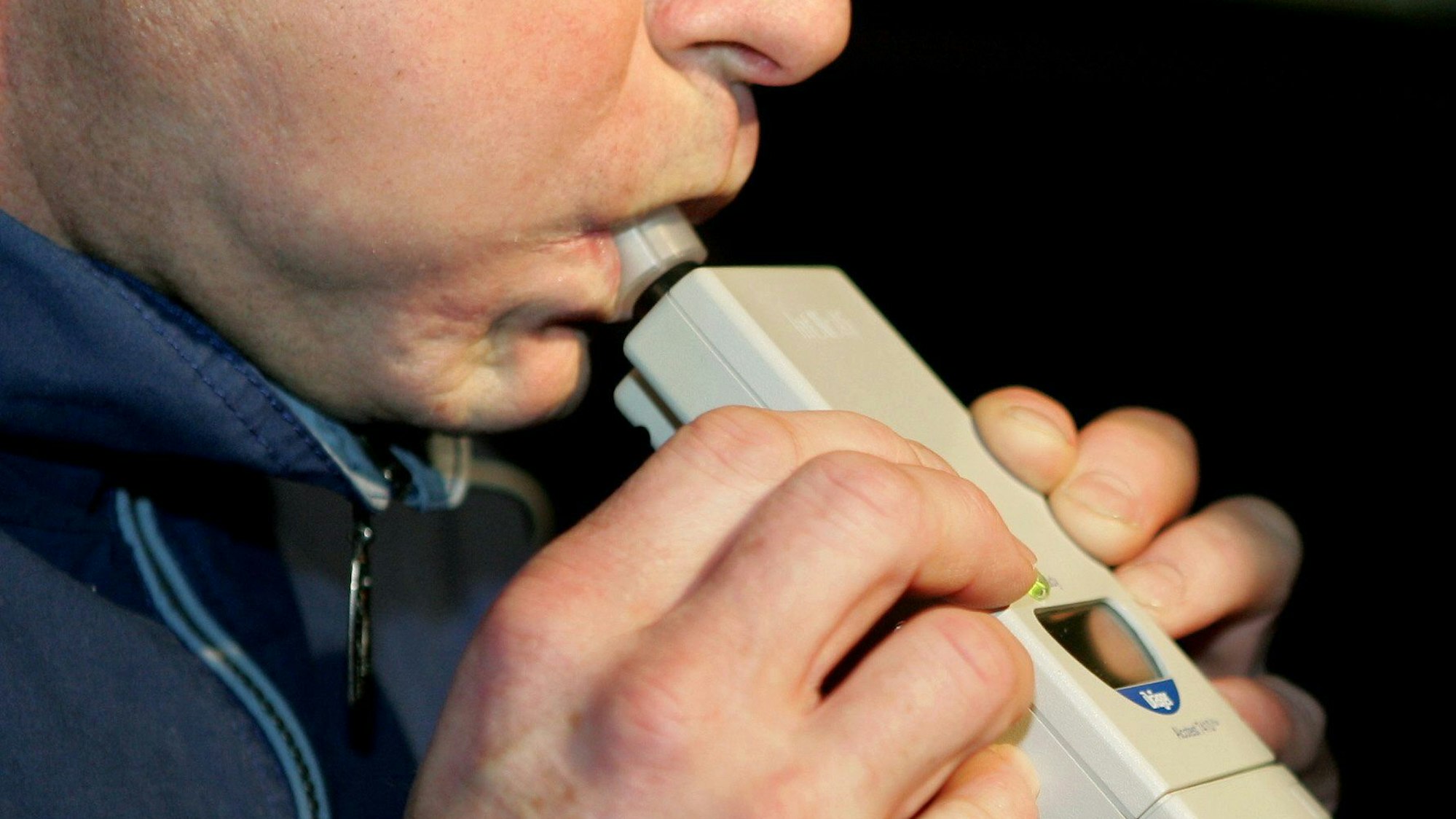 Das Bild zeigt eine Person, die in ein Alkoholtestgerät pustet.