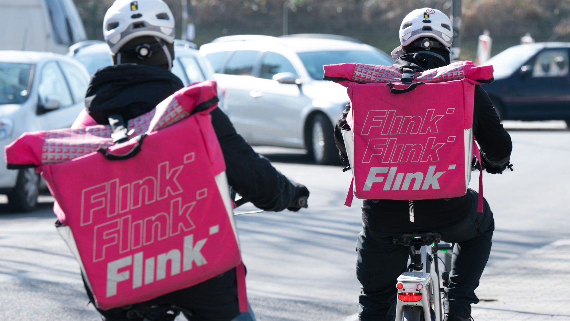 Zwei Fahrradkuriere des Lebensmittel-Lieferdienstes Flink tragen die markanten pinken Taschen des Unternehmens auf ihrem Rücken.