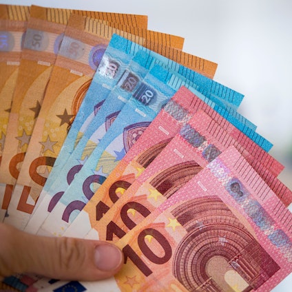 Eine Frau hält Banknoten von 10, 20 und 50 Euro gefächert in der Hand.