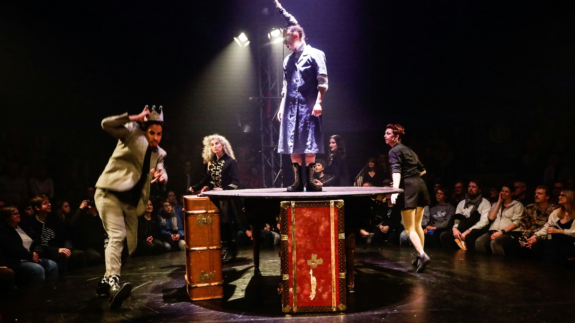 Künstlerinnen und Künstler auf einer runden Bühne um eine Empore herum.