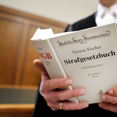 Ein Richter im Gerichtssaal hält das Strafgesetzbuch (StGB) in der Hand.
