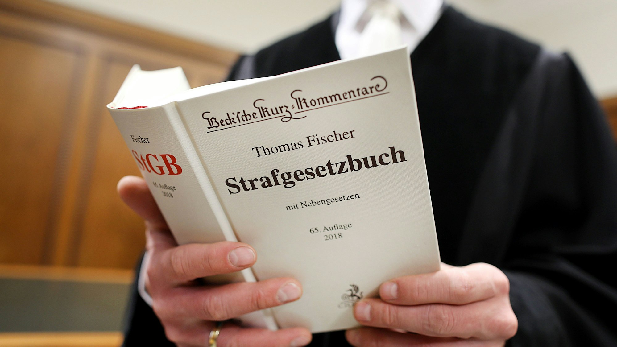 Ein Richter im Gerichtssaal hält das Strafgesetzbuch (StGB) in der Hand.