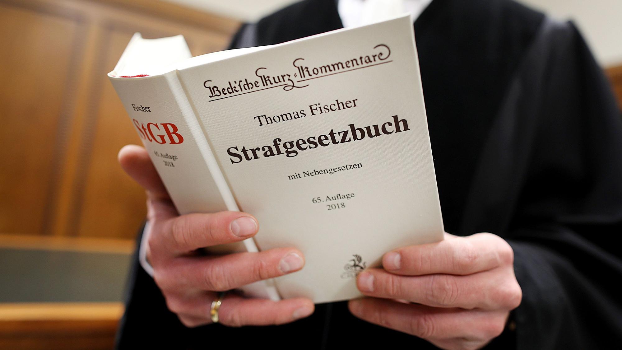 Ein Richter im Gerichtssaal hat das Strafgesetzbuch (StGB) in der Hand.