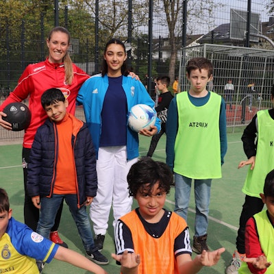 Ex-FC Profispielerin Nina Windmüller steht vor einem Fußballtor umgeben von Kindern in bunten Trikots.
