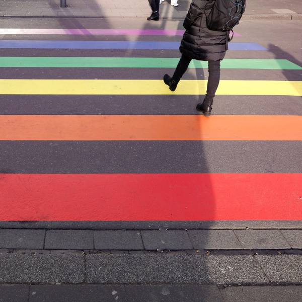 Über einen Zebrastreifen in Regenbogenfarben laufen Menschen.