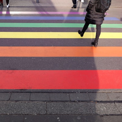 Über einen Zebrastreifen in Regenbogenfarben laufen Menschen.