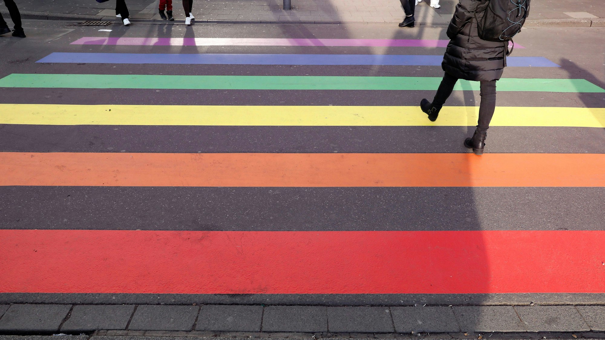 Über einen Zebrastreifen in Regenbogenfarben laufen Menschen.