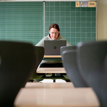 Eine Lehrerin sitzt in ihrem leeren Klassenzimmer vor einem Laptop.