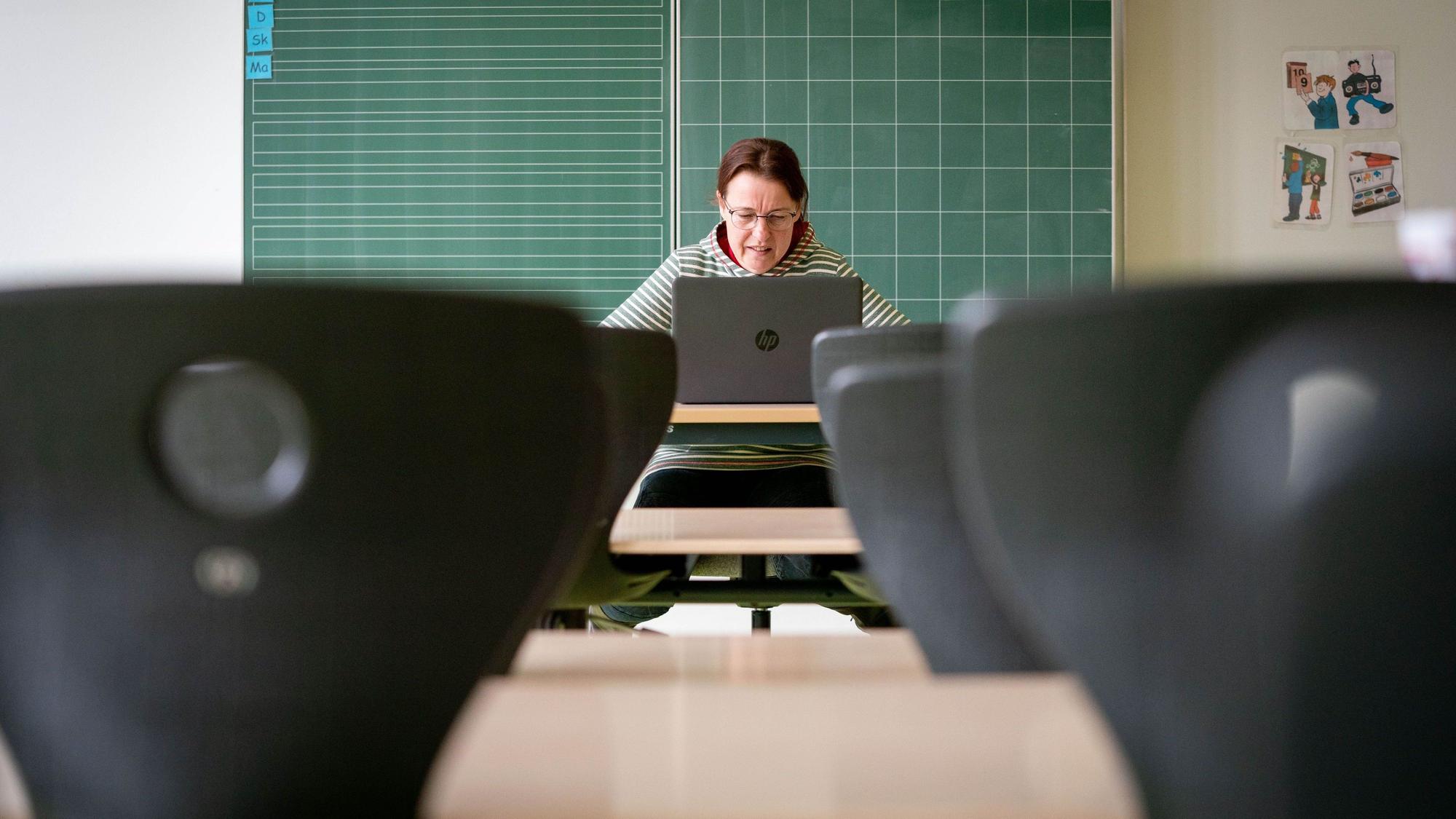 Eine Lehrerin sitzt in ihrem leeren Klassenzimmer vor einem Laptop.