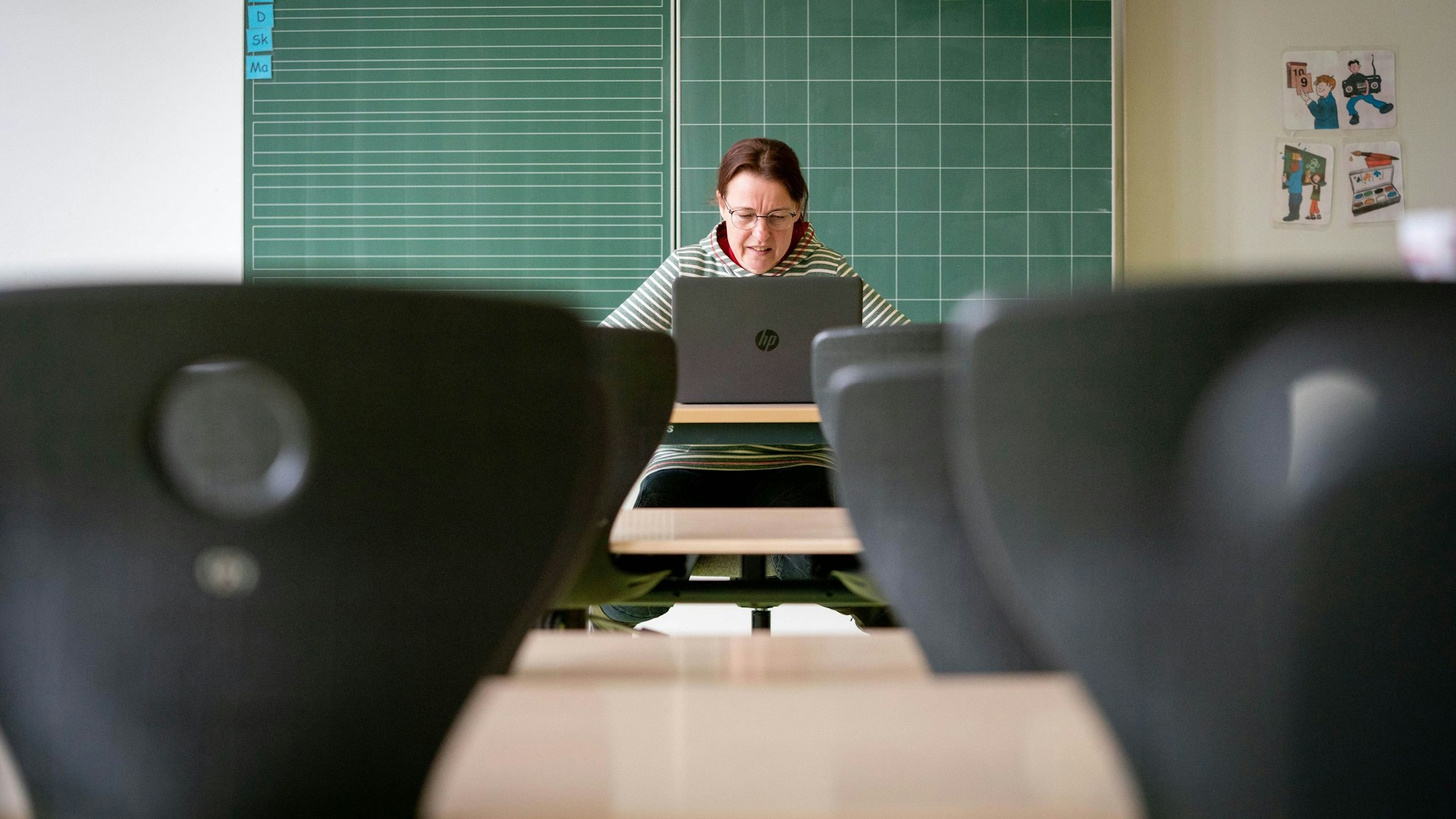 Eine Lehrerin sitzt in ihrem leeren Klassenzimmer vor einem Laptop.