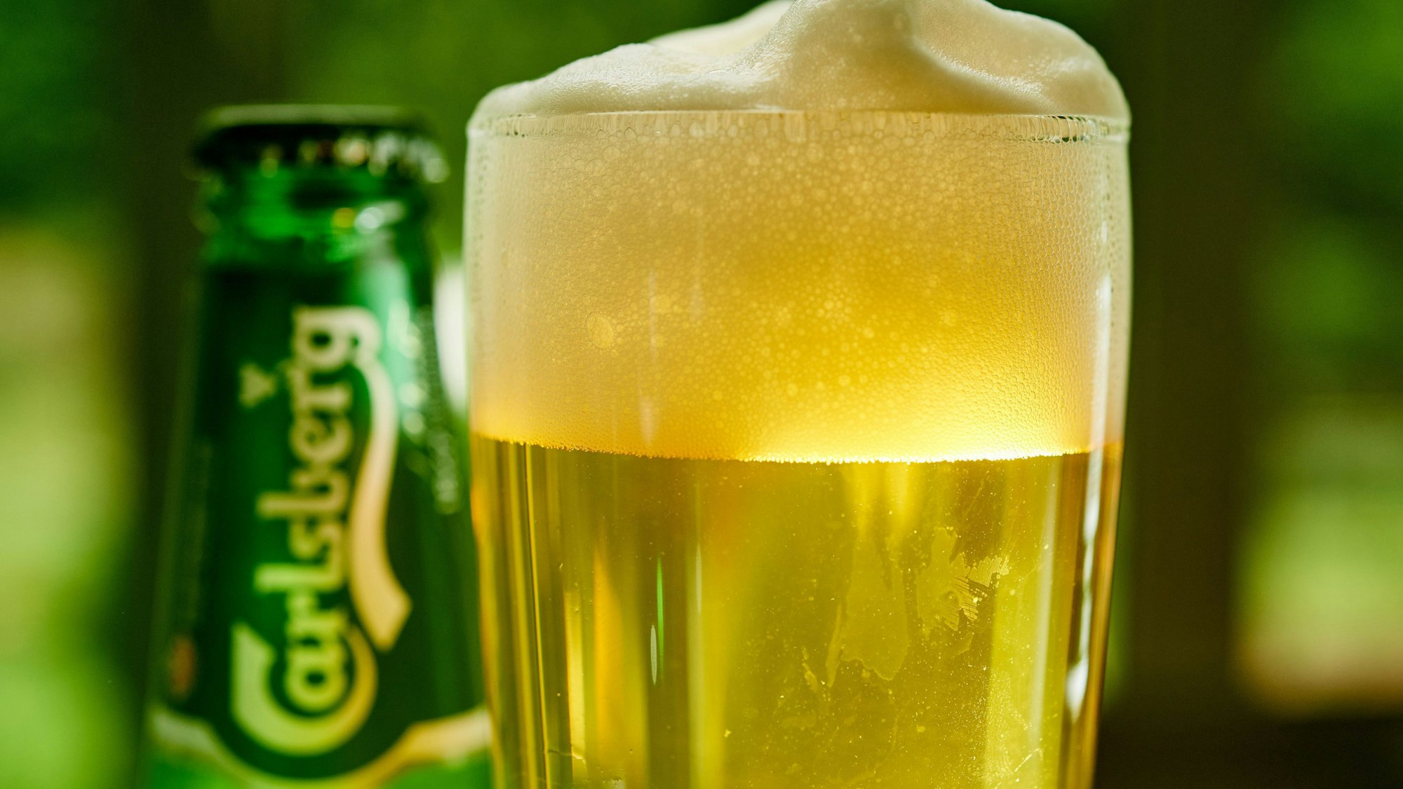 Ein Glas Bier und eine Bierflasche der Marke Carlsberg stehen auf einem Tisch.