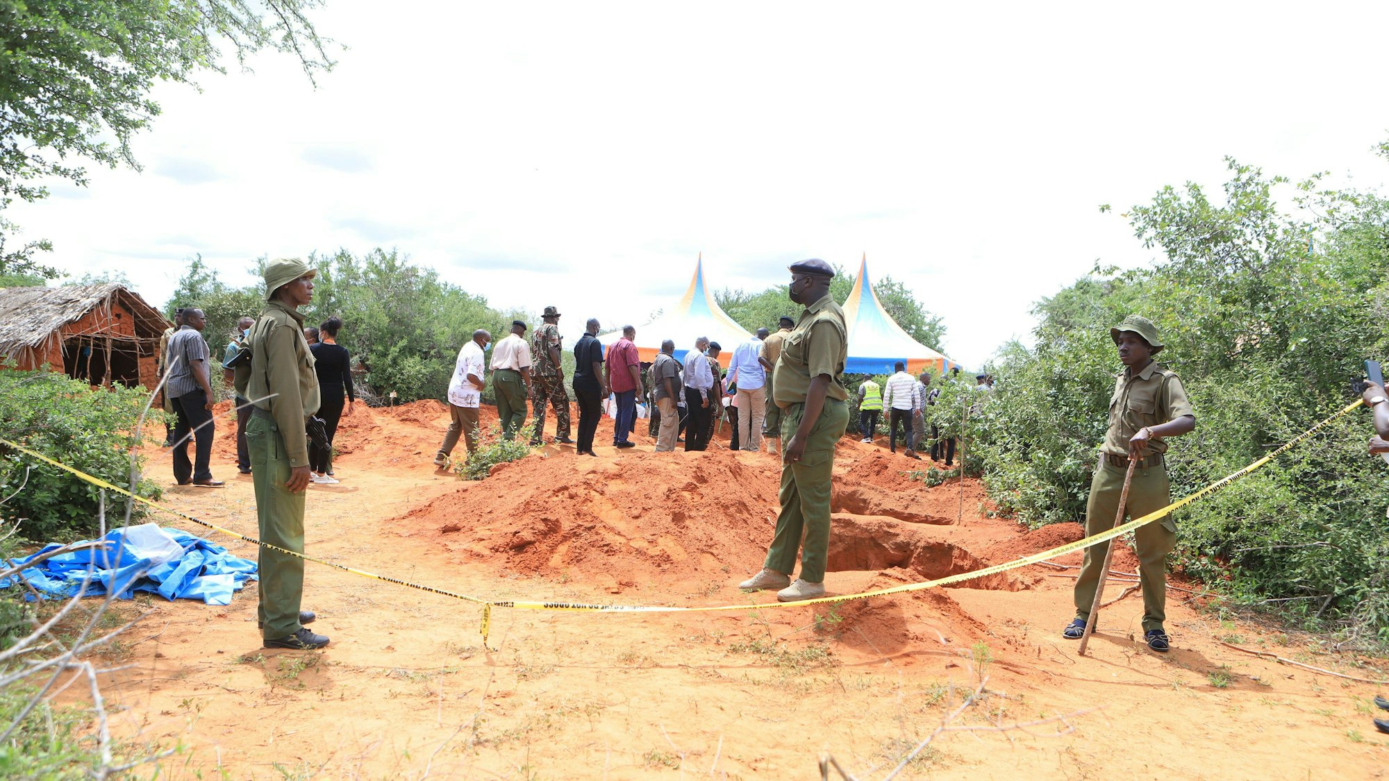 Kenia, Shakahola: Polizeibeamte stehen neben einer Absperrung vor Gräbern, aus denen die Polizei die Leichen von Opfern eines christlichen Sektenkults exhumiert.