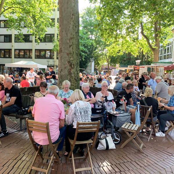 Menschen sitzen an Tischen auf einem Platz.