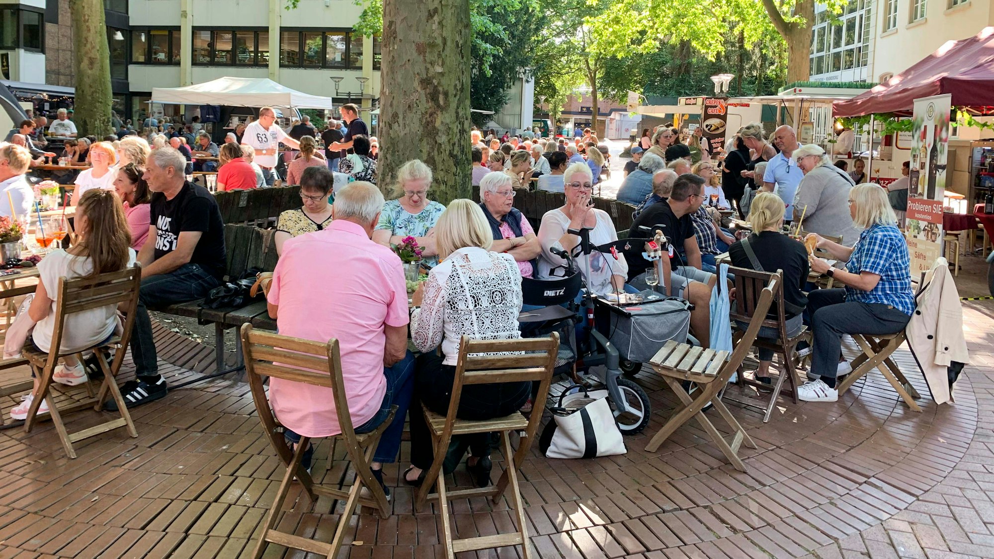 Das Foto zeigt den Schlemmermarkt in Frechen. Besucher sitzen an Tischen und genießen das kulinarische Angebot.