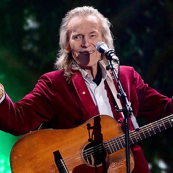 Gordon Lightfoot mit Gitarre auf der Bühne. Er hebt beide Daumen hoch und lacht.