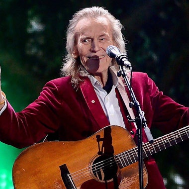 Gordon Lightfoot mit Gitarre auf der Bühne. Er hebt beide Daumen hoch und lacht.