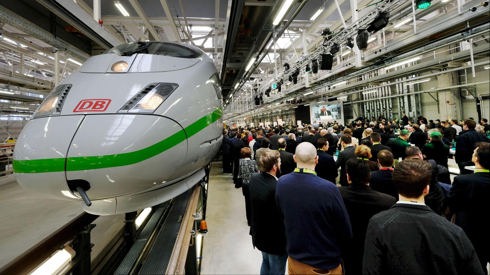 Eröffnung des ICE Werks in Köln-Nippes: Ein neuer ICE-Typ wird präsentiert, viel Publikum ist in einer Werkhalle zu sehen.