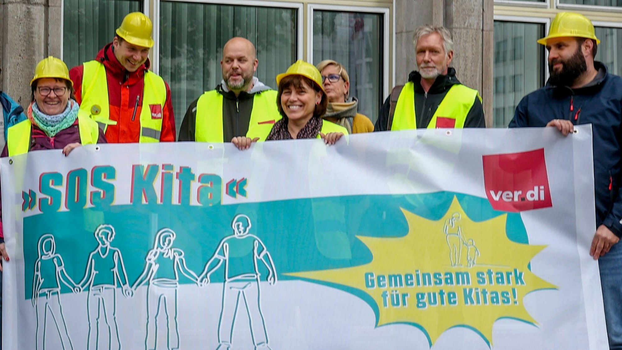Menschen mit gelben Westen und Helm halten ein Banner in der Hand.