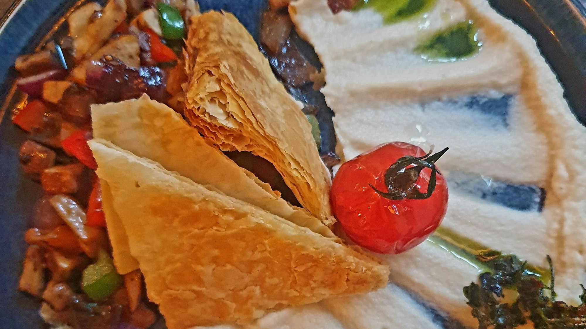 weißes Püree, Gemüse, eine Tomate und Dreiecke aus Blätterteig auf einem Teller