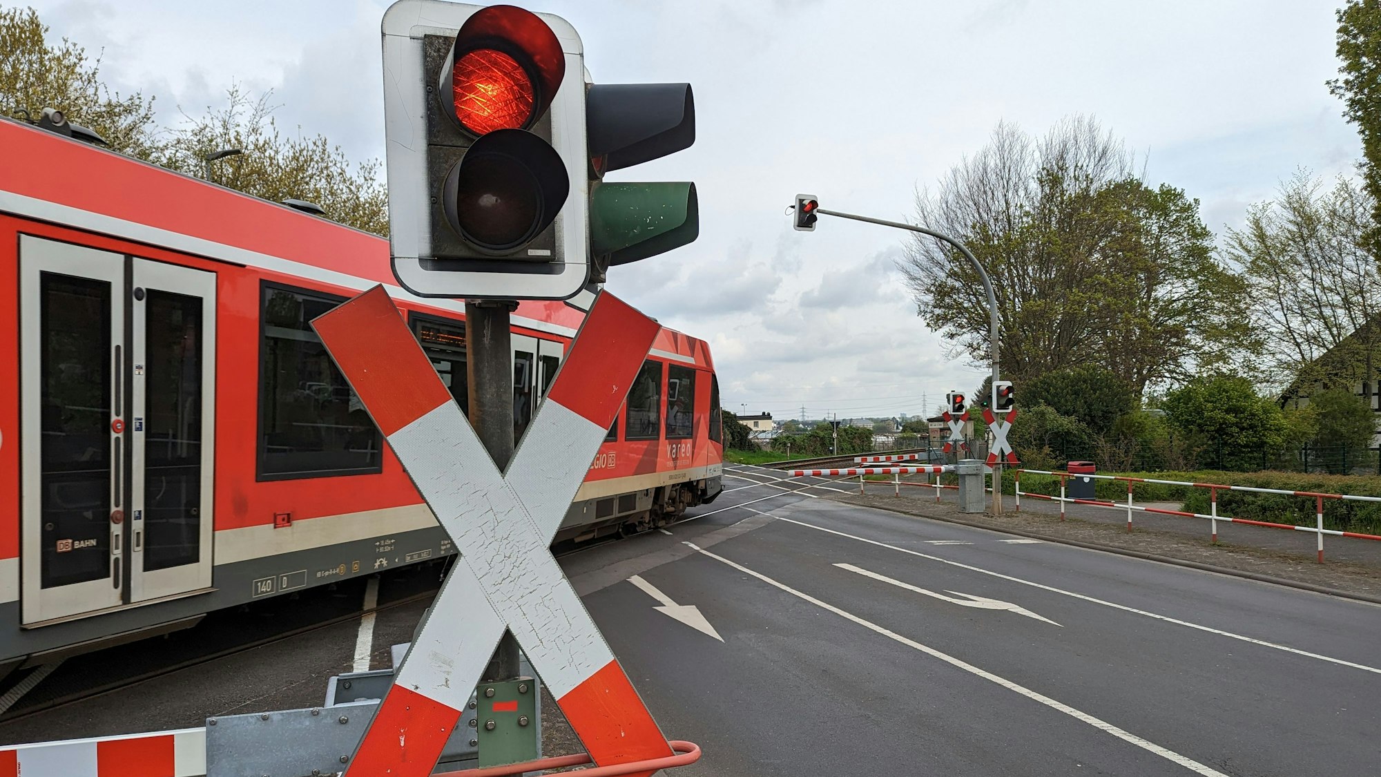Ein Regionalexpress überquert einen Bahnübergang hinter geschlossenen Schranken.