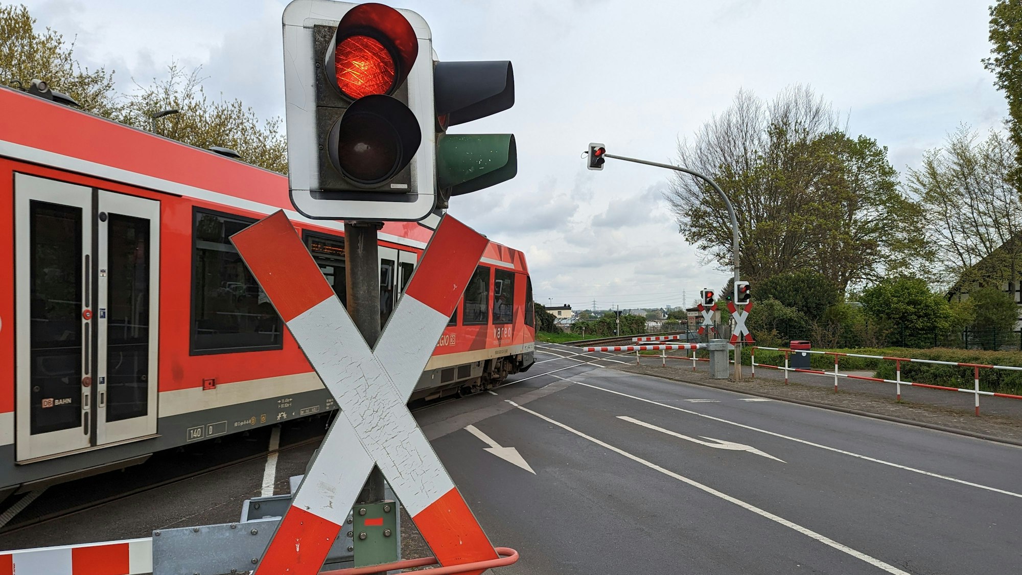 Ein Zug rollt hinter geschlossenen Schranken über den Bahnübergang an der Bonnstraße in Hürth-Fischenich.