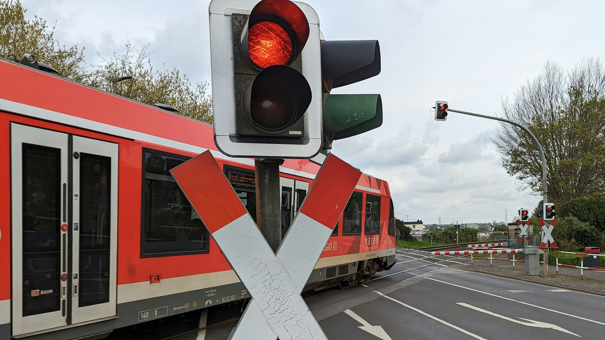 Ein roter Zug der Deutschen Bahn überquert einen Bahnübergang in Hürth.
