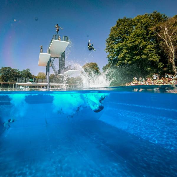 Menschen springen vom Sprungturm im Freibad Stadionbad in Köln ins Wasser.