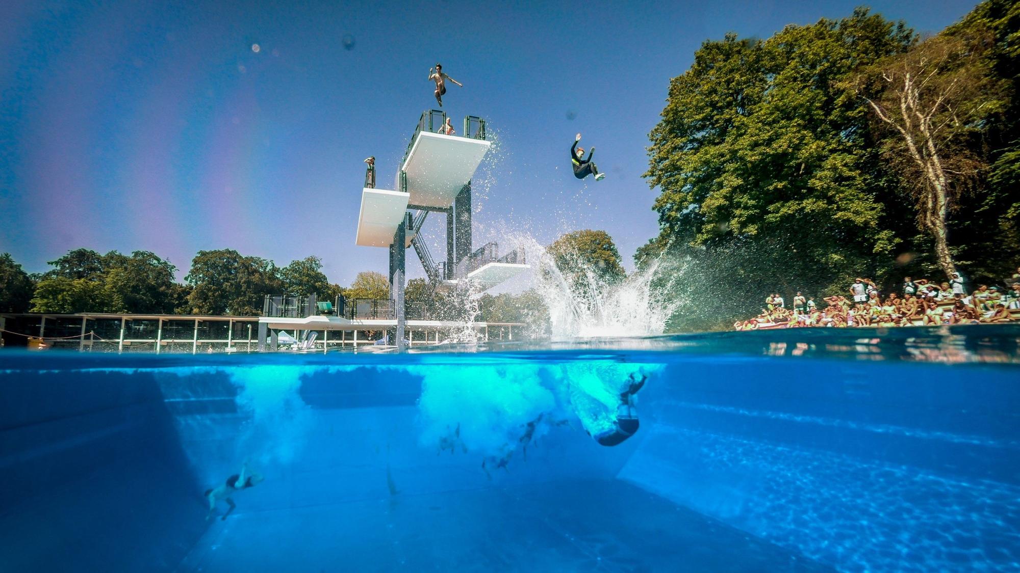 Menschen springen vom Sprungturm im Freibad Stadionbad in Köln ins Wasser.