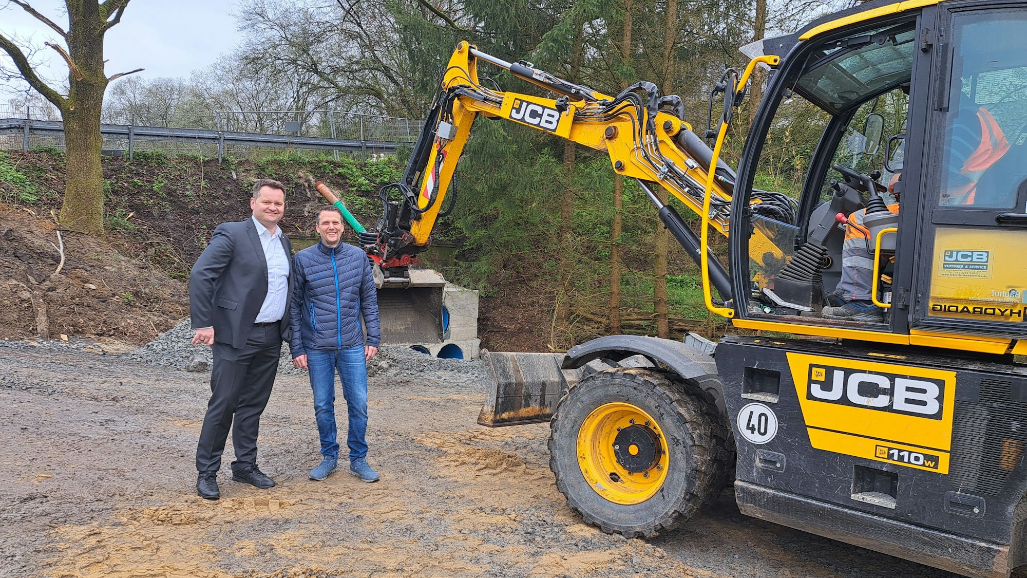Die Sanierung der Brücke in Egerpohl. Zwei Männer schauen in die Kamera, rechts schaufelt ein großer Bagger.
