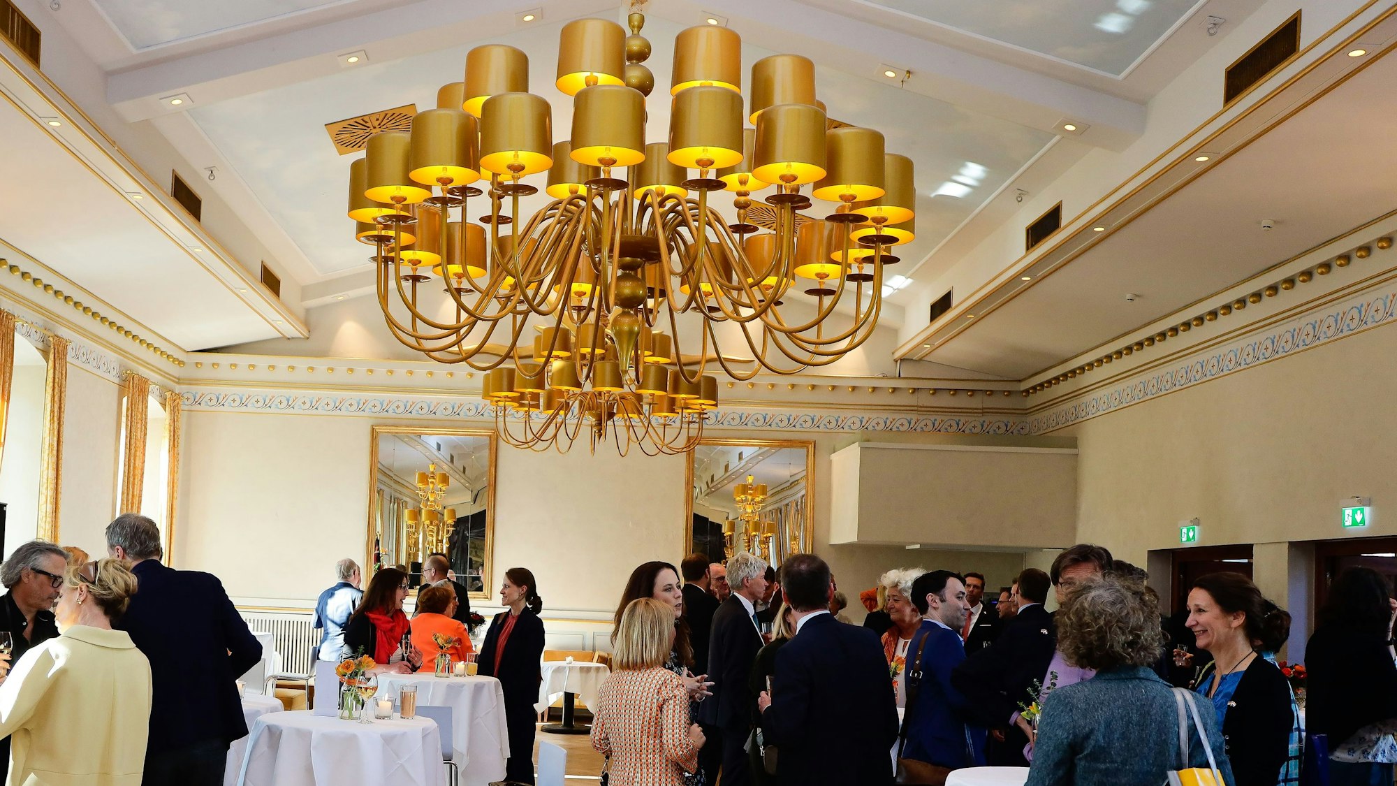 Gäste an Stehtischen in der Wolkenburg unter einem großen Kronleuchter