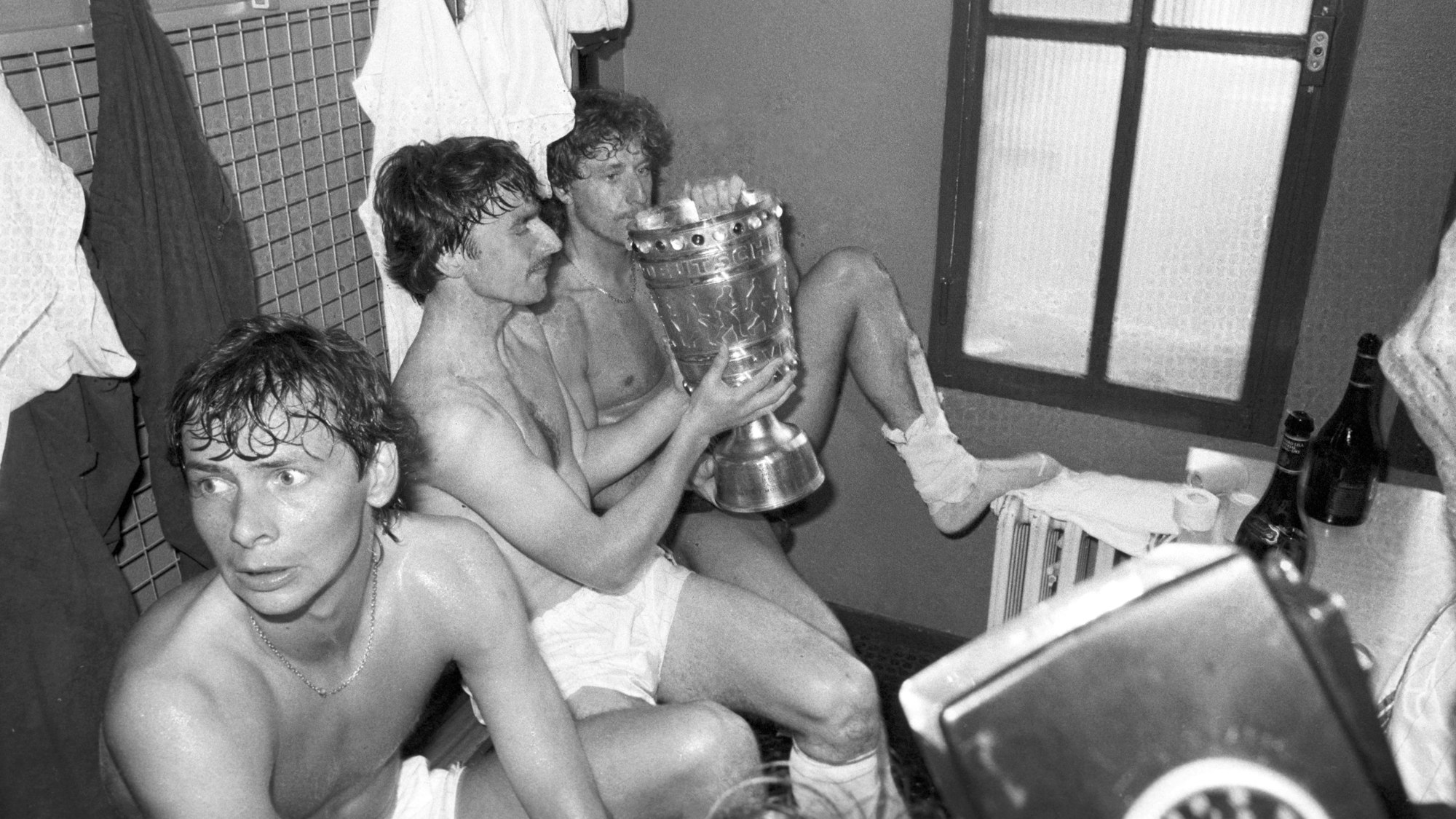 Klaus Allofs (M) und Toni Schumacher (r) vom 1. FC Köln halten am 11.06.1983 den DFB-Pokal in der Umkleidekabine nach dem Finale gegen Fortuna Köln.