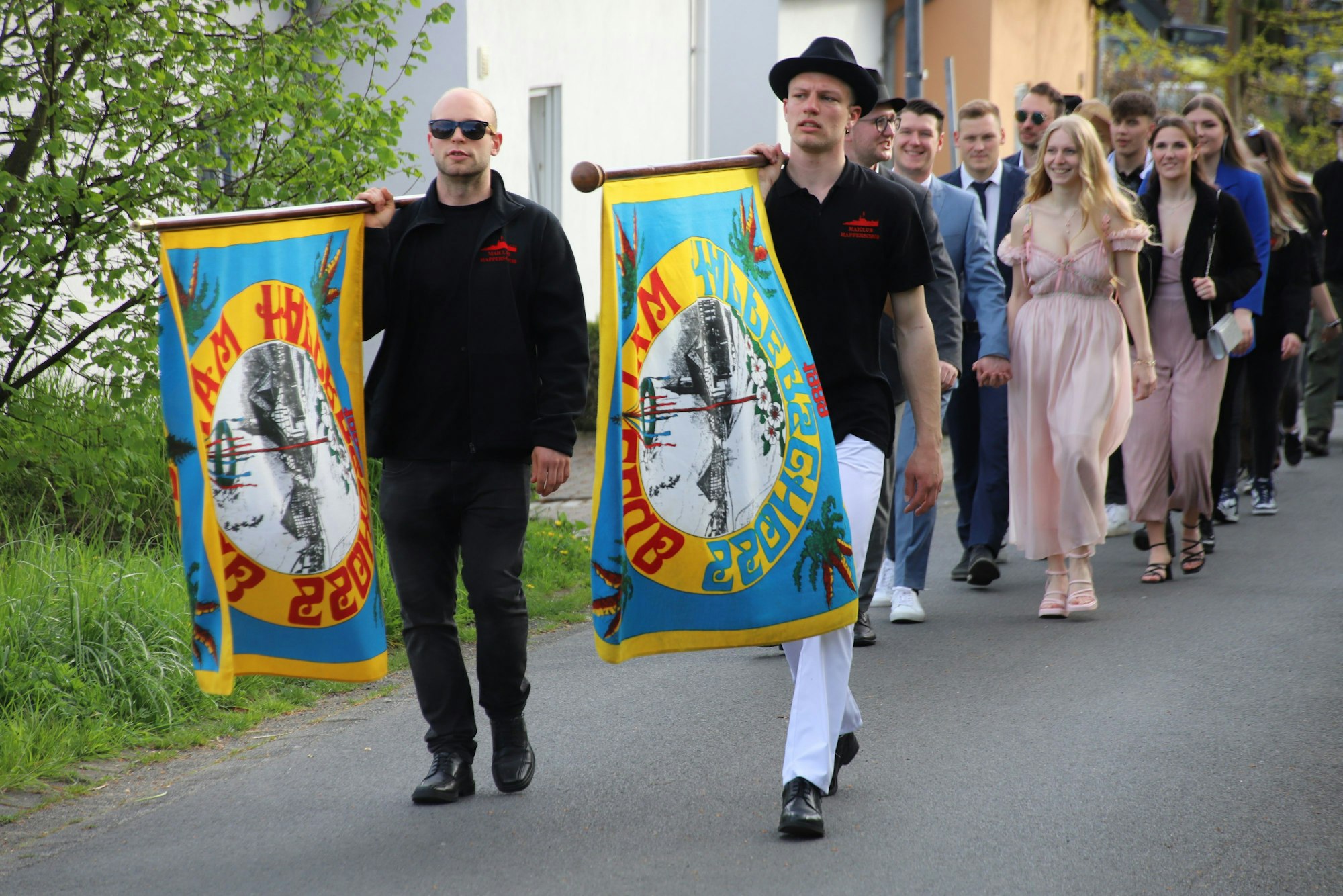 Der Maiclub Happerschoß veranstaltet erstmalig einen Maiumzug: Vorne gehen zwei Männer mit Fahnen, gefolgt von weiteren Zweier-Pärchen in einer Schlange.