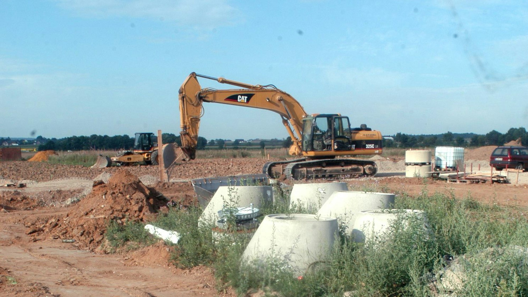 Ein Bagger steht in einem Baugebiet, im Vordergrund liegen Kanalbauteile.