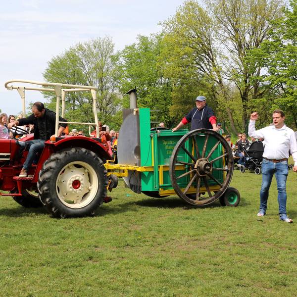Ein roter Traktor zieht eine Gulaschkanone vor Publikum über eine Wiese.