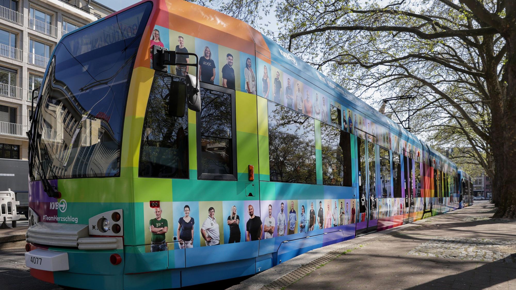 Stehende Straßenbahn, die mit bunten Kacheln und Fotos von KVB-Mitarbeitenden beklebt ist