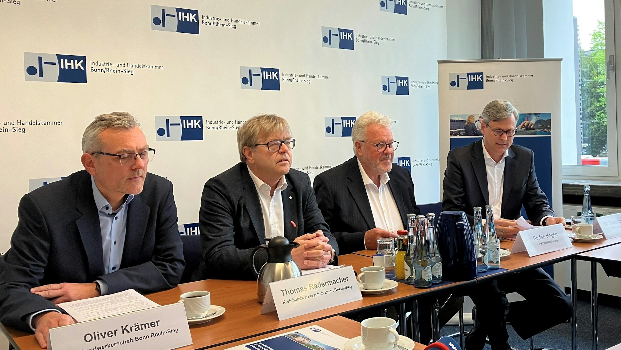 Vier Männer sitzen in Anzügen am Tisch der Pressekonferenz der IHK/KHS.