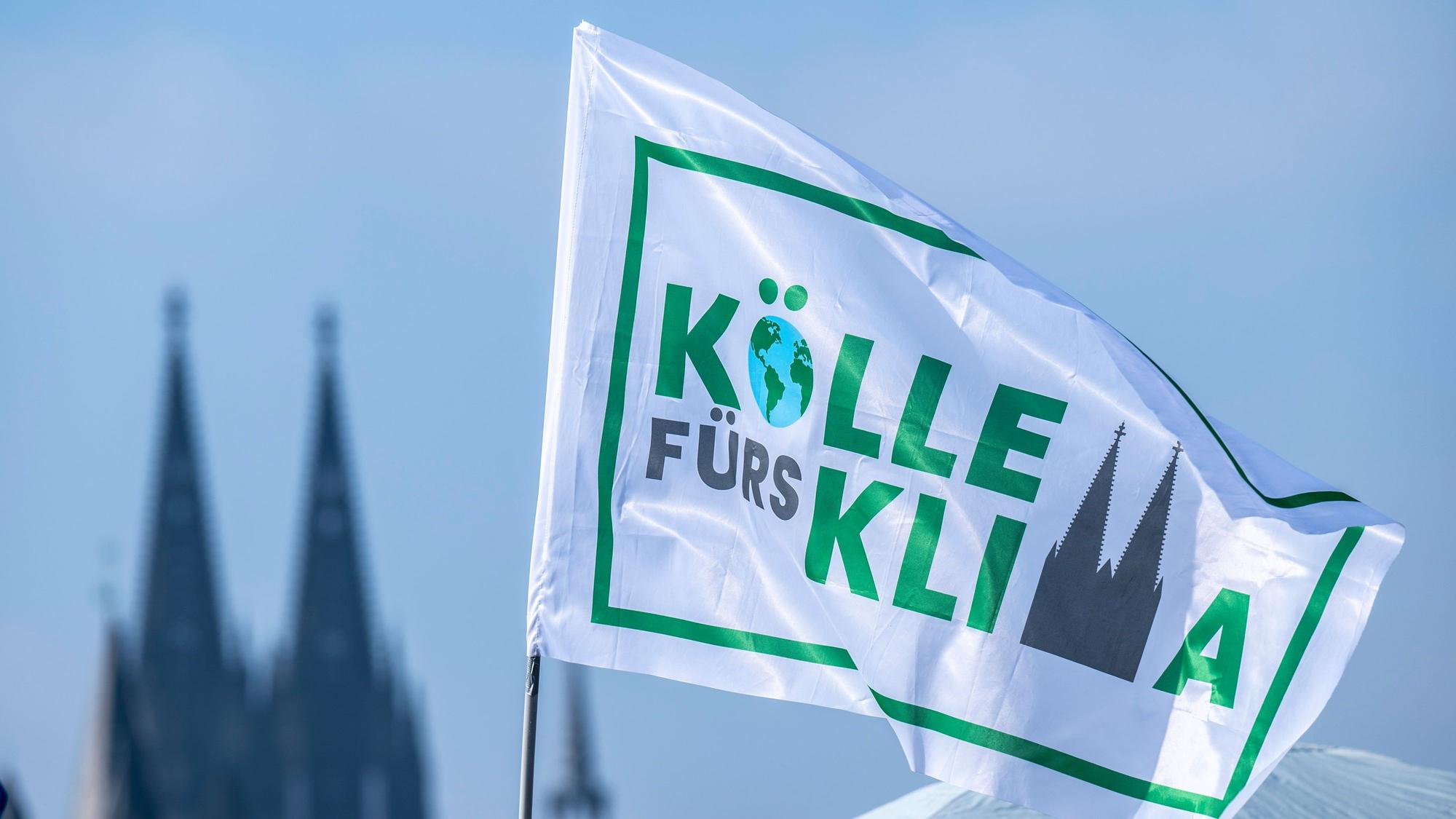 Weiße Fahne „Kölle fürs Klima“ vor dem Himmel, im Hintergrund die Domspitzen