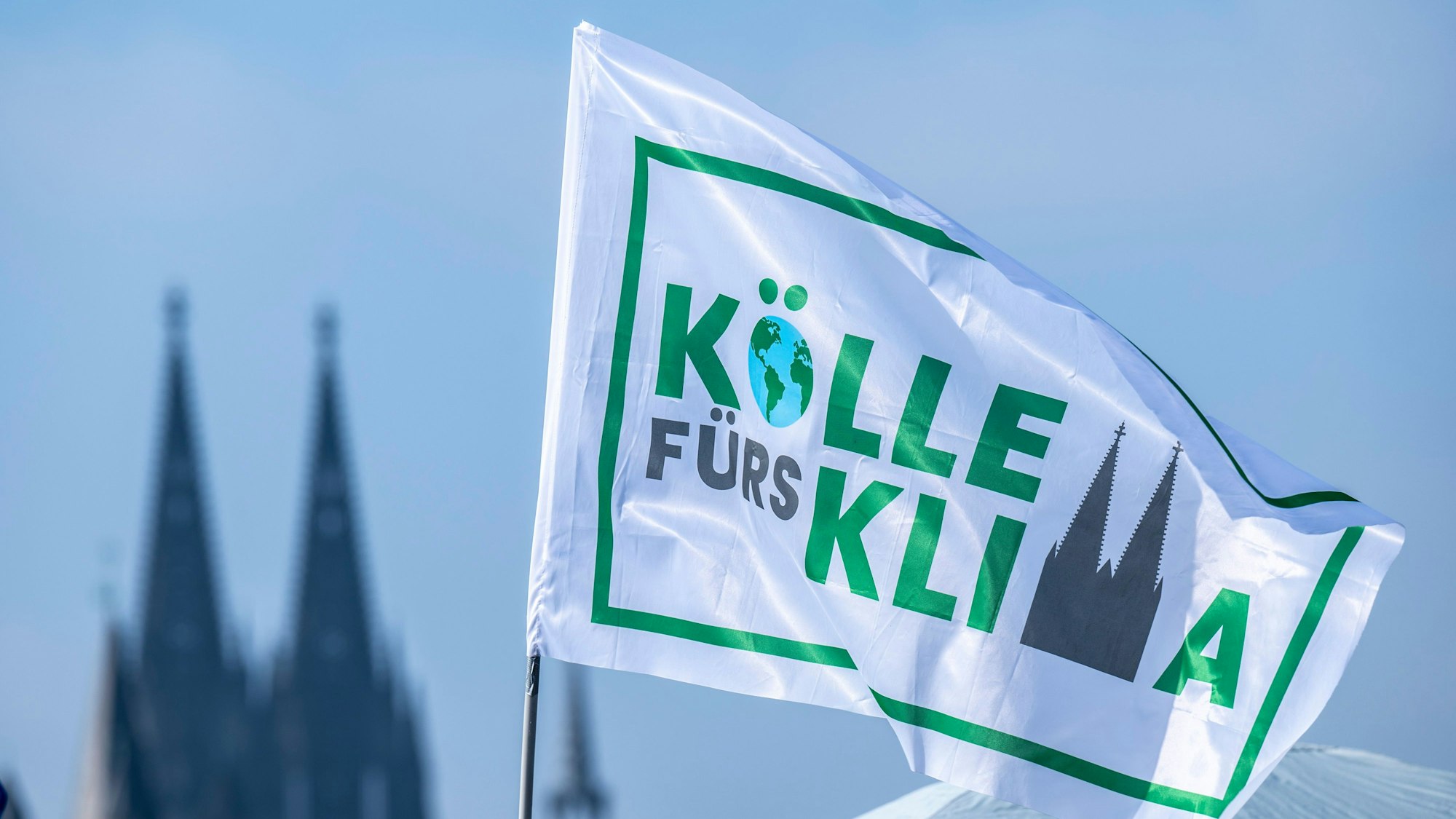 Weiße Fahne „Kölle fürs Klima“ vor dem Himmel, im Hintergrund die Domspitzen
