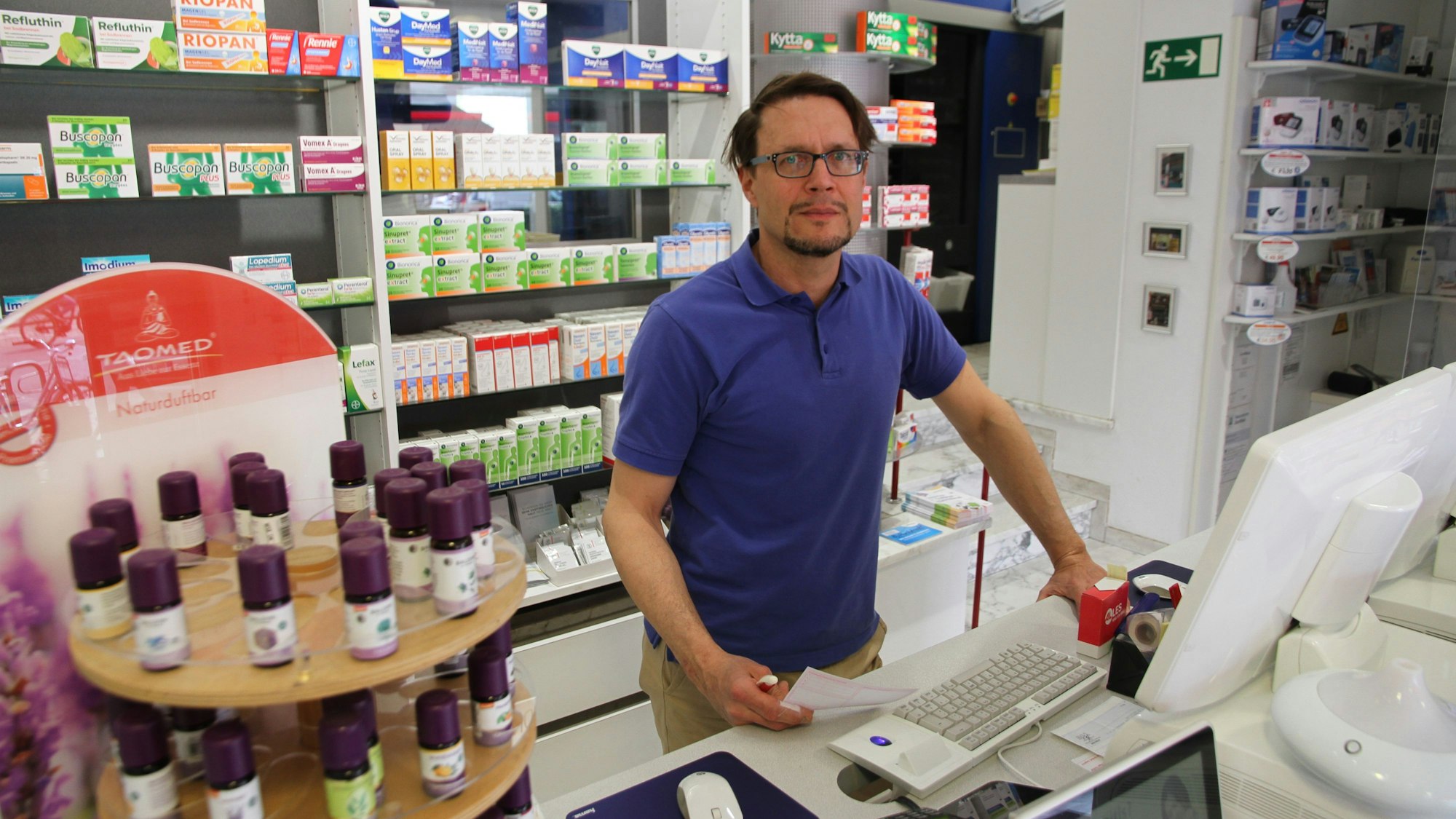 Es ist der Apotheker Marc Remmel zu sehen, wie er hinter seinem Tresen steht.
