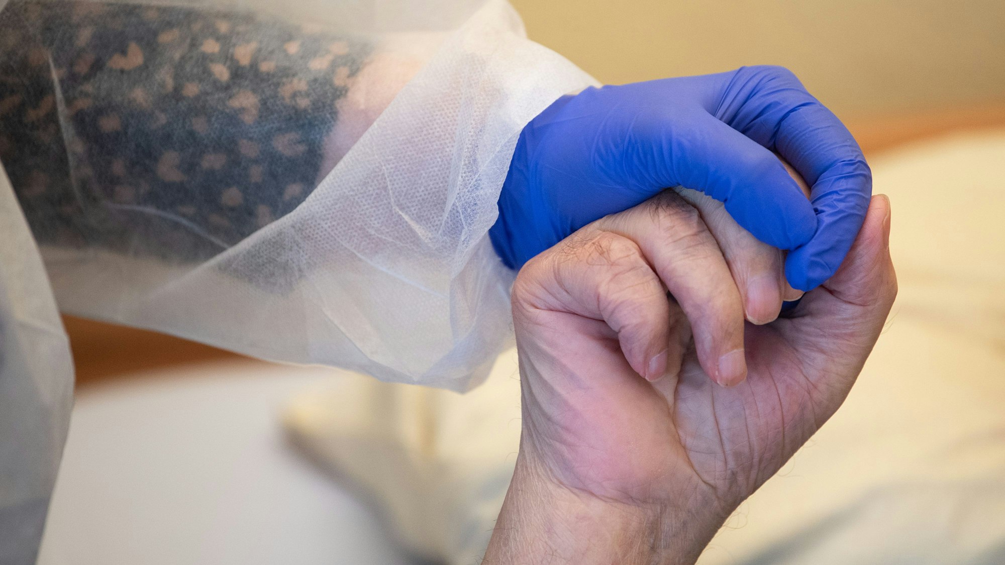 Eine Altenpflegerin in Schutzkleidung hält die Hand eines Bewohners.