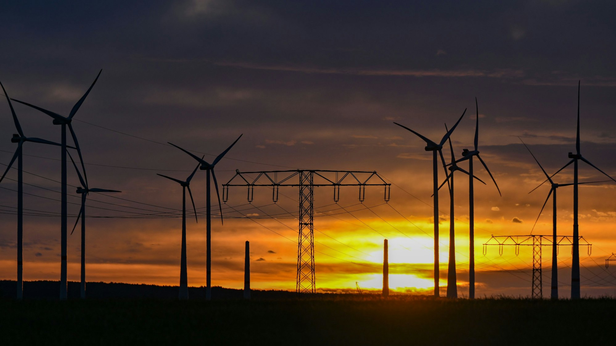 Landschaft mit Windrädern und Strommasten.
