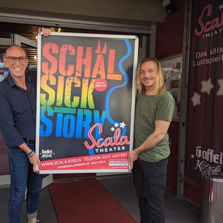 Zwei Männer halten ein Plakat der Theateraufführung hoch.