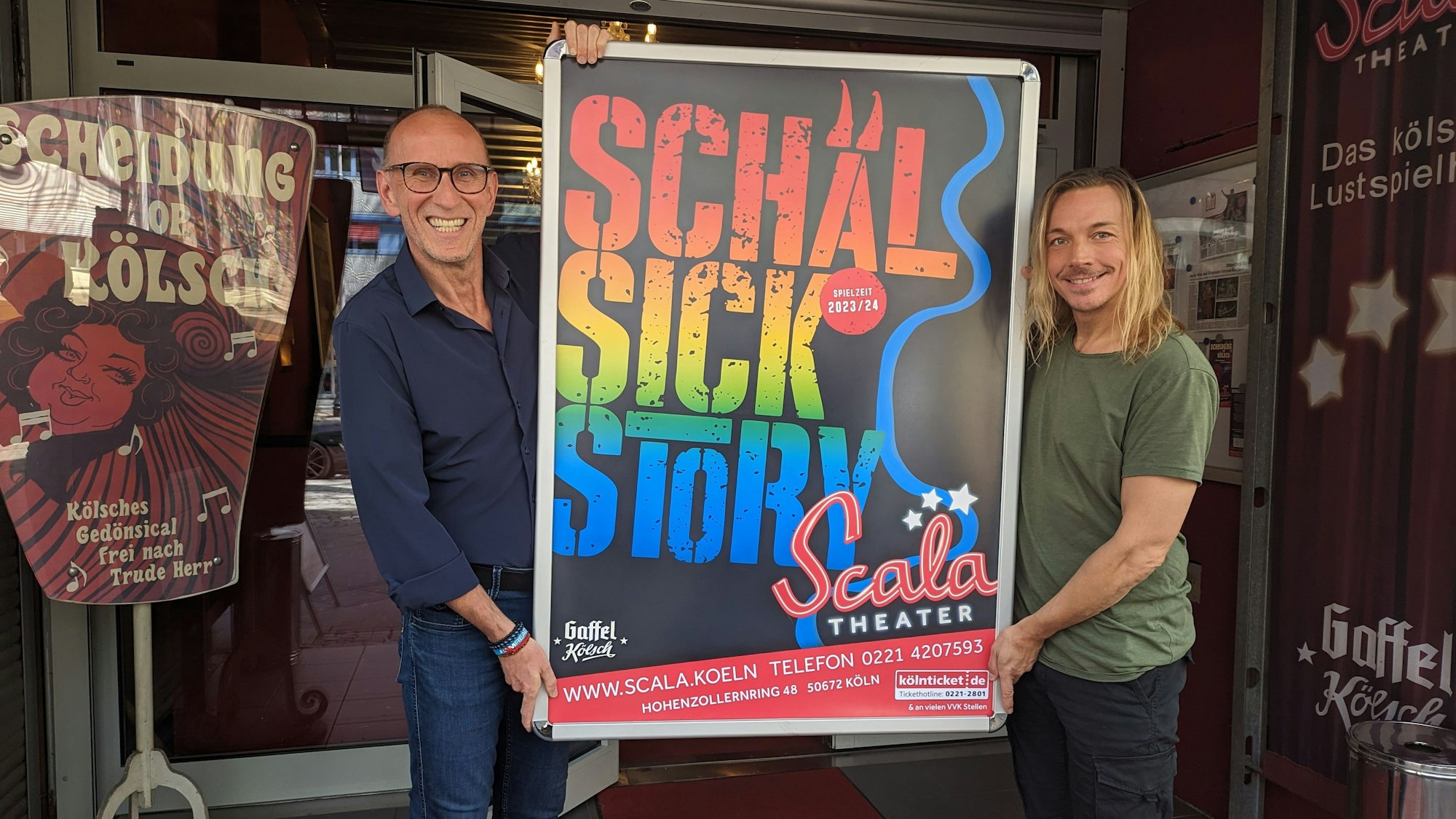 Zwei Männer halten ein Plakat der Theateraufführung hoch.