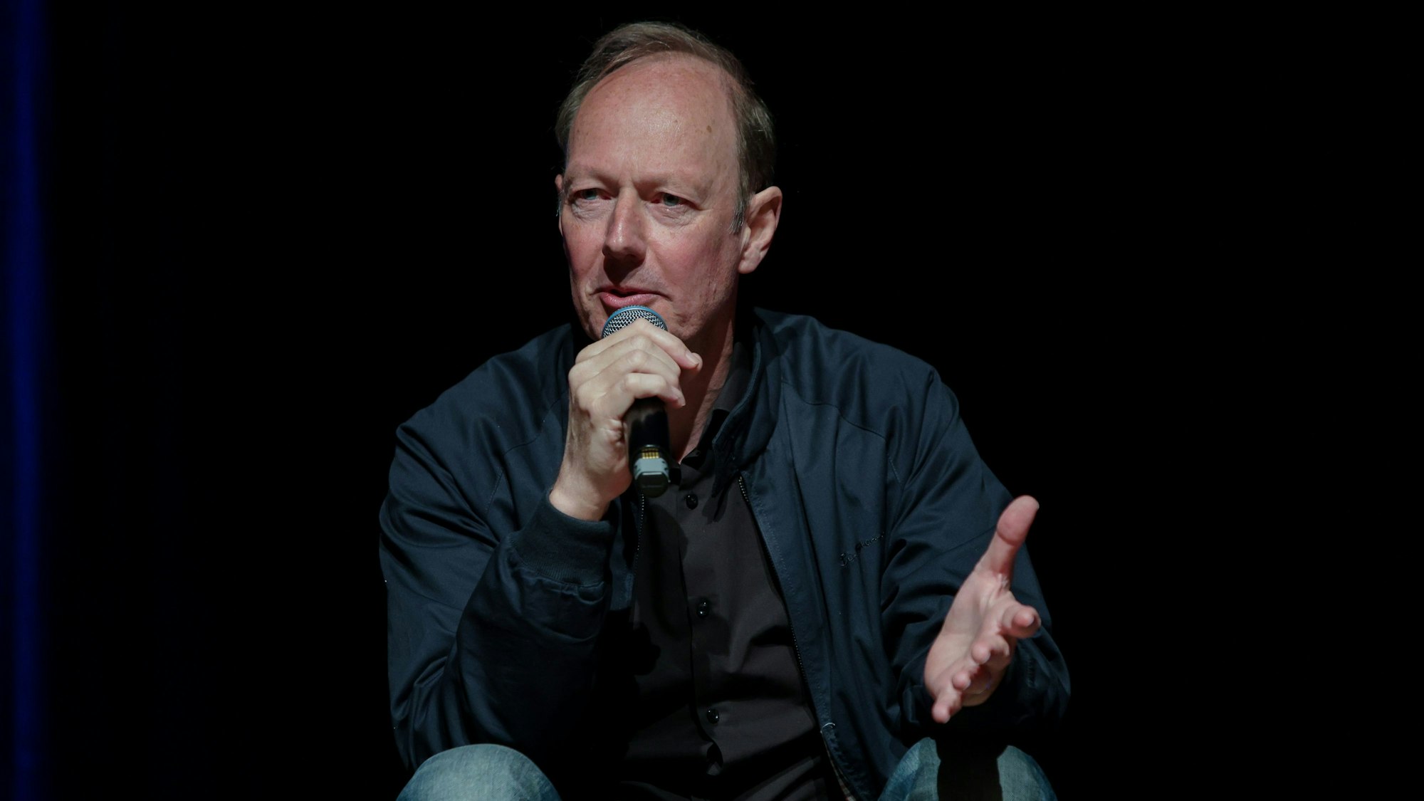 Martin Sonneborn hält ein Mikro in der Hand vor schwarzem Hintergrund und spricht